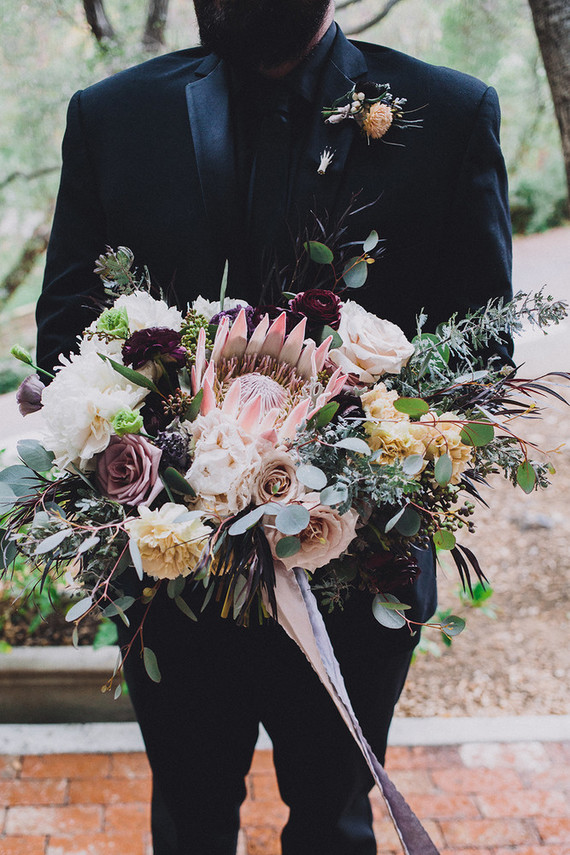 Black groom's suit with protea bouquet