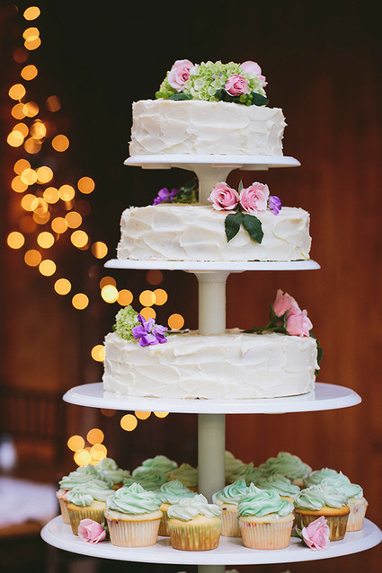 Four tiered white wedding cake with cupcakes